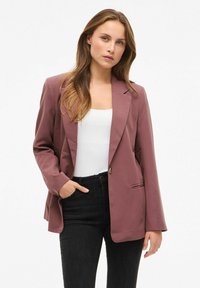 Mauve blejzer s jednim dugmetom, reverima i dugim rukavima; uparen s bijelom majicom i crnim trapericama. Ima detalj bočnih džepova.