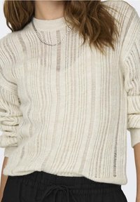 Kremowy sweter z dzianiny w pionowe paski, o luźnym kroju i podwiniętych rękawach. Posiada prążkowany dekolt i przezroczystą teksturę.