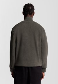 Mörkgrön fleecejacka för män, texturerad tyg, hög krage, ribbade ärmslut och nederkant, avslappnad passform med en slät baksida.