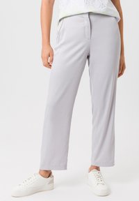 Lichtgrijze rechte broek van gladde stof, met zijzakken en een ontspannen pasvorm, in combinatie met witte sneakers.