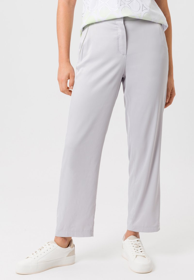 Lichtgrijze rechte broek van gladde stof, met zijzakken en een ontspannen pasvorm, in combinatie met witte sneakers.