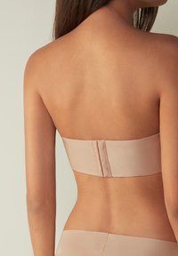 Naakt strapless bh van glad satijnmateriaal, naadband en haaksluiting op de rug. Minimalistisch ontwerp en neutrale kleur.