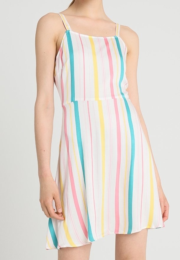 Femme portant une robe sans manches, longueur genoux, avec des rayures verticales en bleu sarcelle, rose, jaune et blanc sur fond clair.