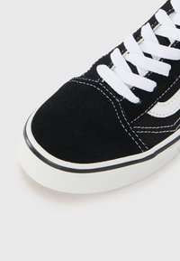 Schwarze Wildleder-Sneaker mit weißen Schnürsenkeln, mit kontrastierenden weißen Nähten und Branding. Gummisohle mit strukturiertem Grip-Detail.