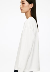 Long-sleeve white T-shirt made of cotton with a relaxed fit, round neckline, and dropped shoulders. Smooth texture, minimal design.