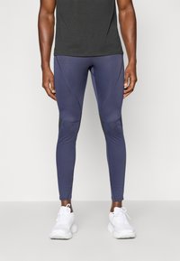 Mallas deportivas de color navy con un diseño ajustado, acentos de paneles contrastantes en negro y un acabado de tela suave y elástica. Combinadas con zapatillas blancas.
