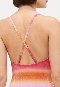 Maillot de bain dégradé rose et orange avec texture pailletée. Dispose de bretelles croisées sécurisées par des anneaux métalliques dans le dos. Fini en tissu lisse.