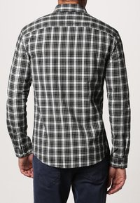 Svartvitt rutigt skjorta med långa ärmar, knapp-down krage och figursydd design. Har en rundad nederkant och knäppte manschetter.