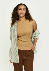 Kreemiga seljaga ribatreeningu särk, mille peal on avatud helesinise triibuga särk, koos pruunide pükstega. Lokilised juuksed raamivad kostüümi.