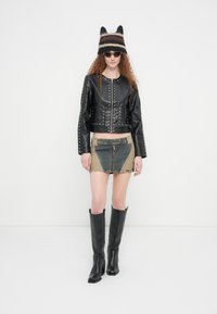 Μαύρο κοντό δερμάτινο μπουφάν με ασημί καρφιά, σε συνδυασμό με γεωμετρική μπεζ και μπλε τζιν μίνι φούστα, και μαύρες ψηλές μπότες με τακούνι μέχρι το γόνατο.