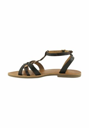 Sandale plate marron avec des lanières en cuir noir croisant à l'avant et une bride à la cheville avec fermeture par boucle sur fond blanc.
