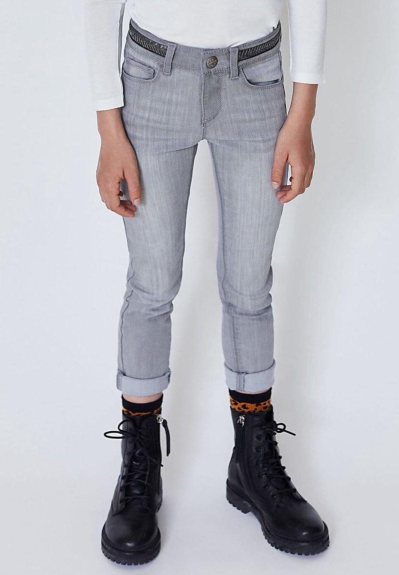 Jean en denim gris à coupe slim, avec ourlets retroussés aux chevilles, doté d'une ceinture noire tissée et de poches avant, assorti à des bottes noires à lacets.
