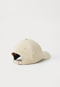Gorra beige hecha de tela texturizada. Cuenta con un visor curvado, una correa ajustable en la parte posterior y un diseño de seis paneles con orificios de ventilación.