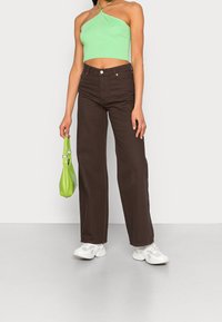 Brązowe jeansy z wysokim stanem i szerokimi nogawkami, zestawione z zielonym crop topem na ramiączkach i białymi trampkami. Dopełnione małą zieloną torebką.