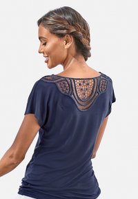 Kornblumenblaues T-Shirt mit kurzen Ärmeln, das ein Häkelrücken-Design und eine lockere Passform bietet. Weicher Stoff mit glatter Textur und abgerundetem Saum.