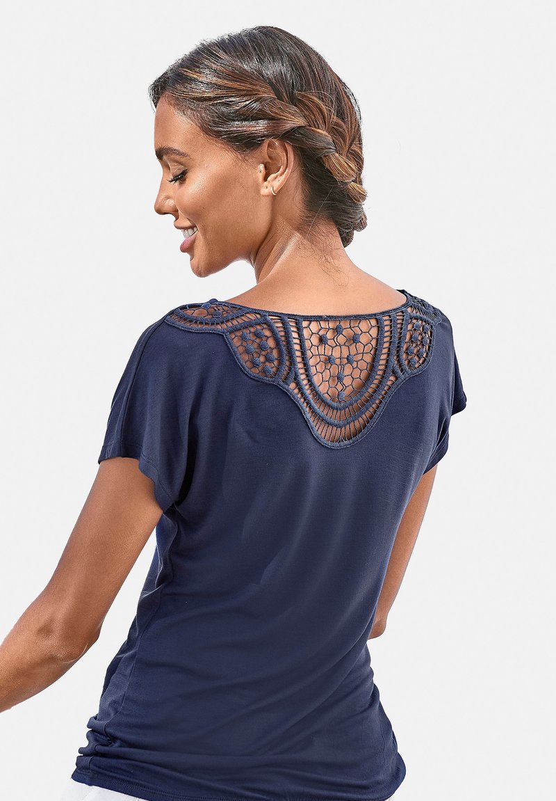 Kornblumenblaues T-Shirt mit kurzen Ärmeln, das ein Häkelrücken-Design und eine lockere Passform bietet. Weicher Stoff mit glatter Textur und abgerundetem Saum.