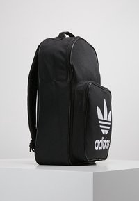 Black backpack made of durable fabric, featuring a large front pocket with a white Adidas logo, and padded straps for comfort.