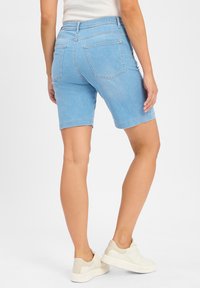 Lichtblauwe denim short met een rechte snit, vijf zakken en een iets uitgerafelde zoom, gecombineerd met witte lage schoenen.