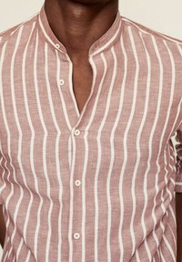 Camisa de manga corta en rosa claro con rayas verticales blancas, con cuello de banda y cierre de botones, hecha de tejido texturizado.