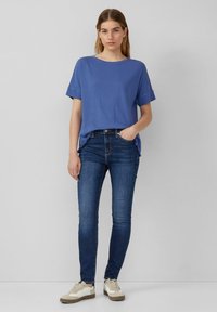 Niebieska bawełniana koszulka z krótkim rękawem, w połączeniu z ciemnoniebieskimi skinny jeansami i beżowymi sneakersami. Prosty, codzienny zestaw o luźnym kroju.