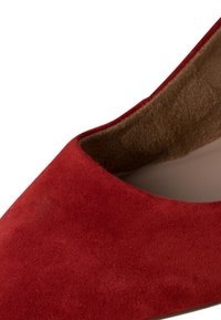 Zapato de tacón alto de ante rojo con punta afilada y forro interior suave. Presenta un diseño clásico y una textura suave.