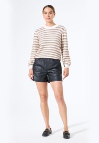 Suéter de punto negro y crema a rayas con mangas abullonadas, combinado con pantalones cortos de cuero negros de cintura alta. Mocasines negros completan el conjunto.