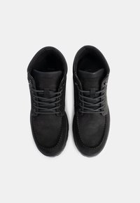 Zapatos de cuero negros con punta redonda, costuras en contraste y cordones grises, con una textura suave y un collar acolchado.