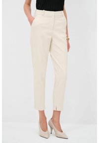 Beige šité kalhoty se slim fit střihem, bočními kapsami a délkou po kotníky. Materiál je hladký s přehybem vpředu pro upravený vzhled.