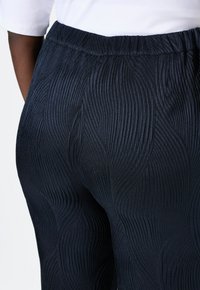 Marineblaue, gefaltete Hose mit elastischem Bund, ausgestattet mit einem strukturierten Wellenmuster und einem glatten, weichen Finish.