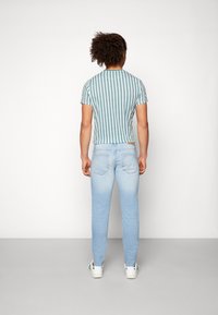 Pasiasta zielono-biała koszulka w połączeniu z jasnoniebieskimi skinny jeansami, uzupełniona białymi trampkami. Materiał wydaje się lekki i swobodny.