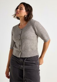 Grå, kortærmet cardigan i blødt strik med rund halsudskæring og fem mørke knapper. Ribbet kant ved taljen.