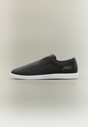 Μαύρο sneaker slip-on με λευκή σόλα, επάνω μέρος από λείο δέρμα και χρυσή επιγραφή "Lacoste" στο πλάι και στη γλώσσα.