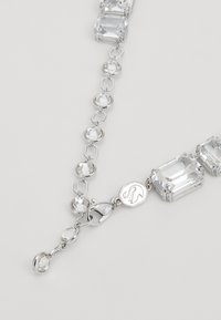 Silver chain necklace featuring clear rectangular and round crystals, with hexagonal links and a clasp displaying a logo detail.