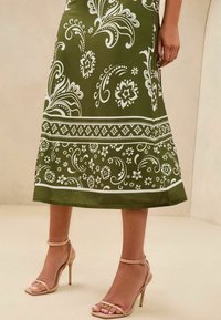 Fustă verde măsliniu cu modele florale albe, cu un design evazat și accente pe margine. Asortată cu sandale cu toc nude, cu bretele.