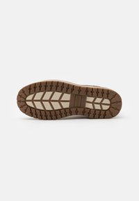 Semelle de chaussure en caoutchouc marron avec un motif de bande de roulement texturé, comportant des rainures et des sections surélevées pour l'adhérence et la traction.