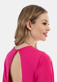 Abito fucsia a maniche lunghe con dettaglio a apertura a chiave sul retro, caratterizzato da una texture liscia e un accento in hardware dorato sul colletto.