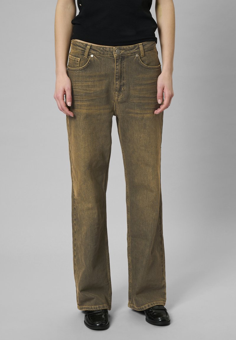 Brązowe dżinsy o luźnym kroju, pięciokieszeniowym wzorze i subtelnych zagięciach. Posiadają wysoki stan i prosty krój nogawki, zestawione z czarnymi butami.