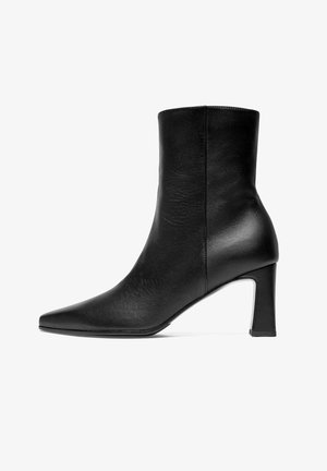 Botte de cheville en cuir noir avec un bout pointu, texture lisse, design ajusté et un talon carré modéré. Silhouette simple et élégante.