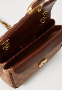Brown leather handbag with a textured light brown patterned fabric. Features a gold-toned clasp and chain strap. Interior with card slots.