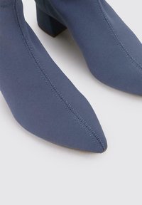 Bottes chevilles en tissu texturé bleu, design à bout pointu, talon carré, avec des coutures visibles et une finition lisse.