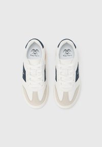 Poros baltų sportinių batelių su smėlio spalvos ir tamsiai mėlynomis detalėmis, surištos raišteliais, žvelgiant iš viršaus ant vientisos baltos spalvos fono.