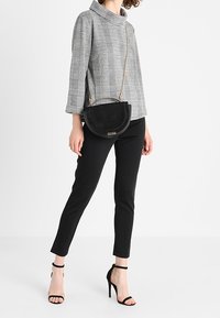 Gray plaid top with a funnel neck, paired with black slim-fit pants. Black suede crossbody bag with a circular shape and gold chain strap.