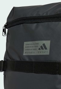 Schwarzer, robuster Stoffrucksack mit einem oberen Reißverschluss, verstellbarem Tragegurt und einem Markenetikett mit geografischen Koordinaten.