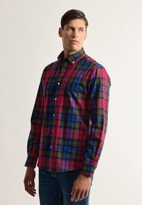 Camisa de cuadros roja, azul y verde con cuello, mangas largas y detalles de bolsillo en la parte delantera, combinada con jeans azules.