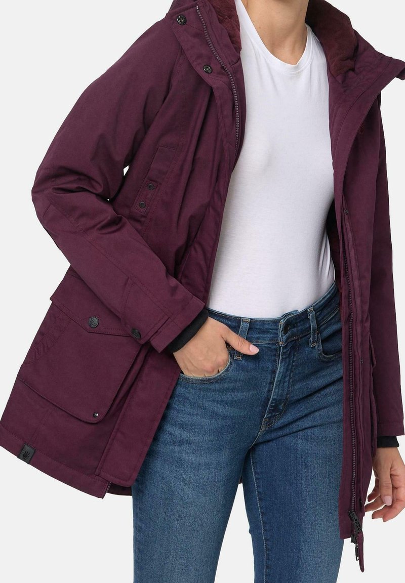 Giacca color marrone scuro con chiusura con zip e bottoni a pressione, dotata di colletto foderato in pelliccia, molteplici tasche e vestibilità comoda. Abbinata a jeans blu.