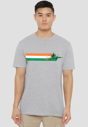 Man wearing gray t-shirt with a graphic of a superhero flying horizontally over orange, white, and green stripes.