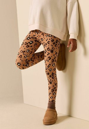 Rudos tamprės su juodu leopardžio raštu, derinamos su rudais užmaunami batais ir šviesios spalvos per didelio dydžio džemperiu.