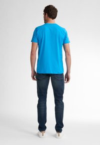 Světle modré bavlněné tričko s kulatým výstřihem, ve spojení s tmavými džínami a bílými teniskami s béžovým akcentem na patě.