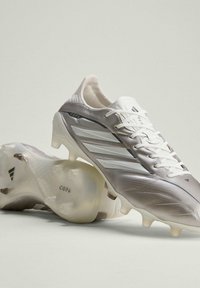 Chaussures de football Adidas Copa argentées et blanches avec crampons moulés, lacets attachés, vues de côté et de la semelle sur un fond clair.