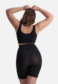 Zwart naadloos sportoutfit bestaande uit een aansluitende bralette en high-waisted shorts. Gladde textuur, geribbelde details en geen zichtbare naden.